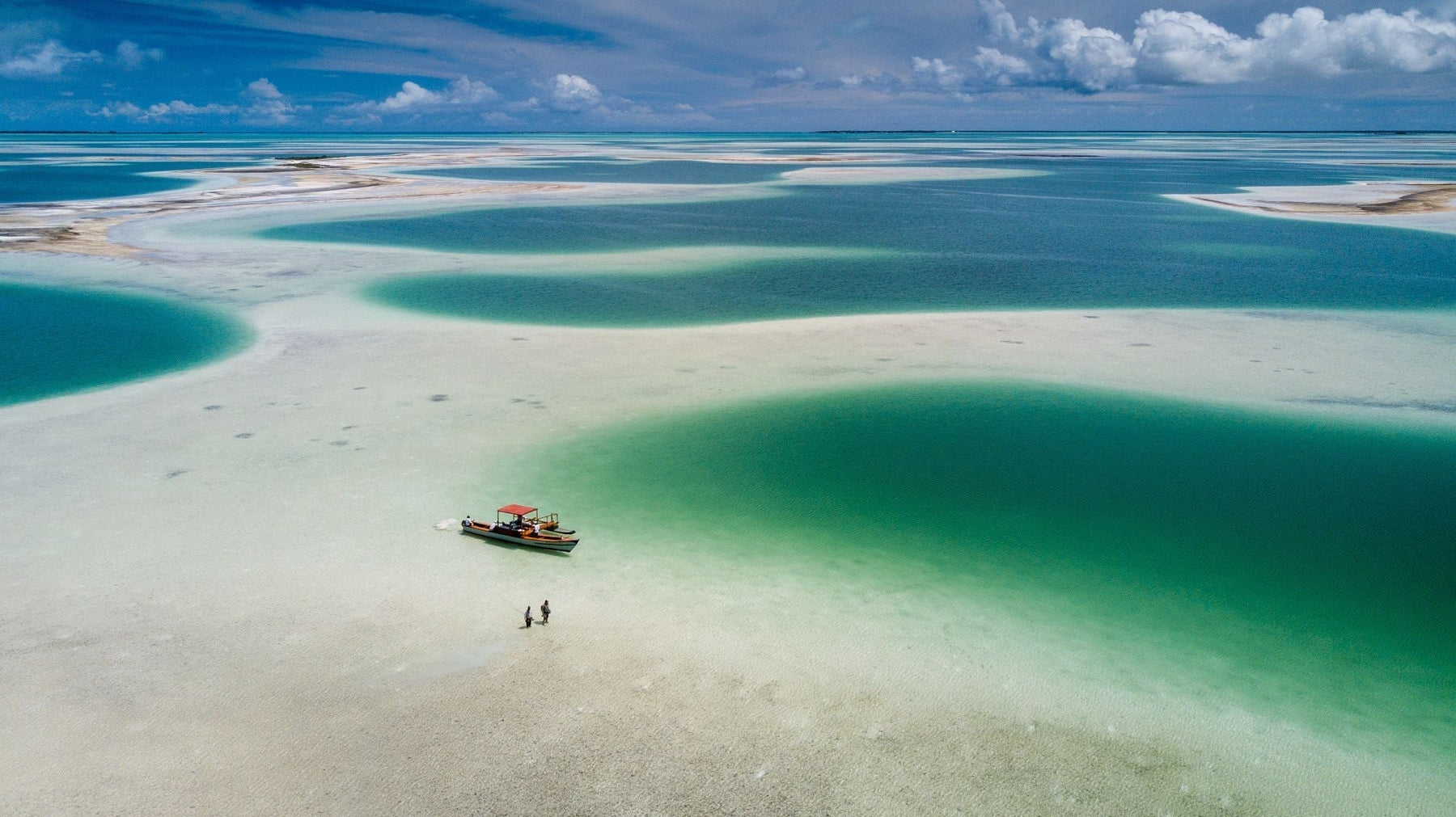 Aerial view of a boat and two fly fishers wading across turquoise flats at Christmas Island