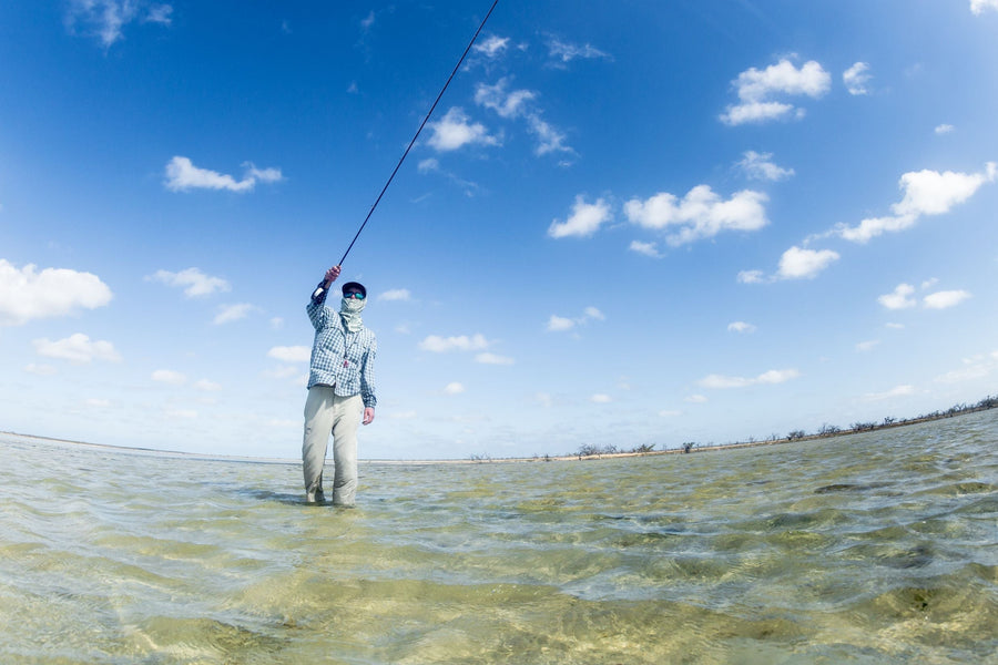 Angler fly fishing and casting while wading in shallow clear flats under a bright blue sky