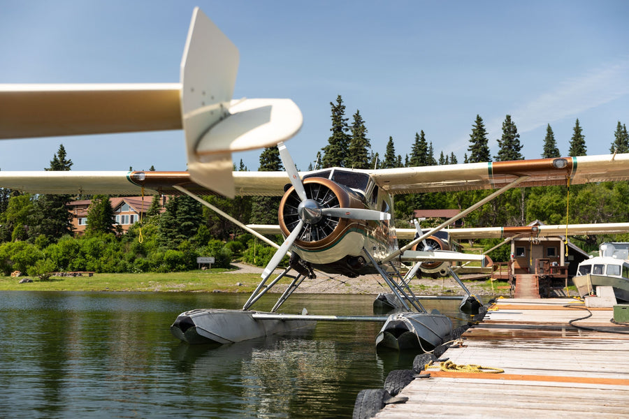 Seaplane parked at a wooden dock on a tree-lined lake near cabins, ready for a fly-fishing trip