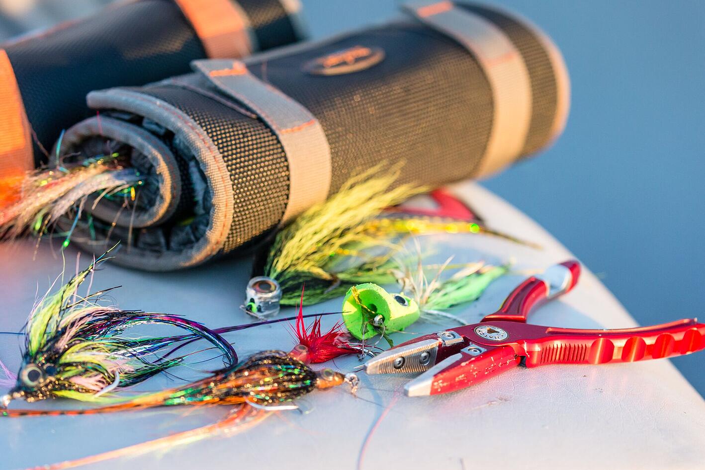 Close-up of red fly fishing pliers showcasing serrated jaws with colorful saltwater flies and gear