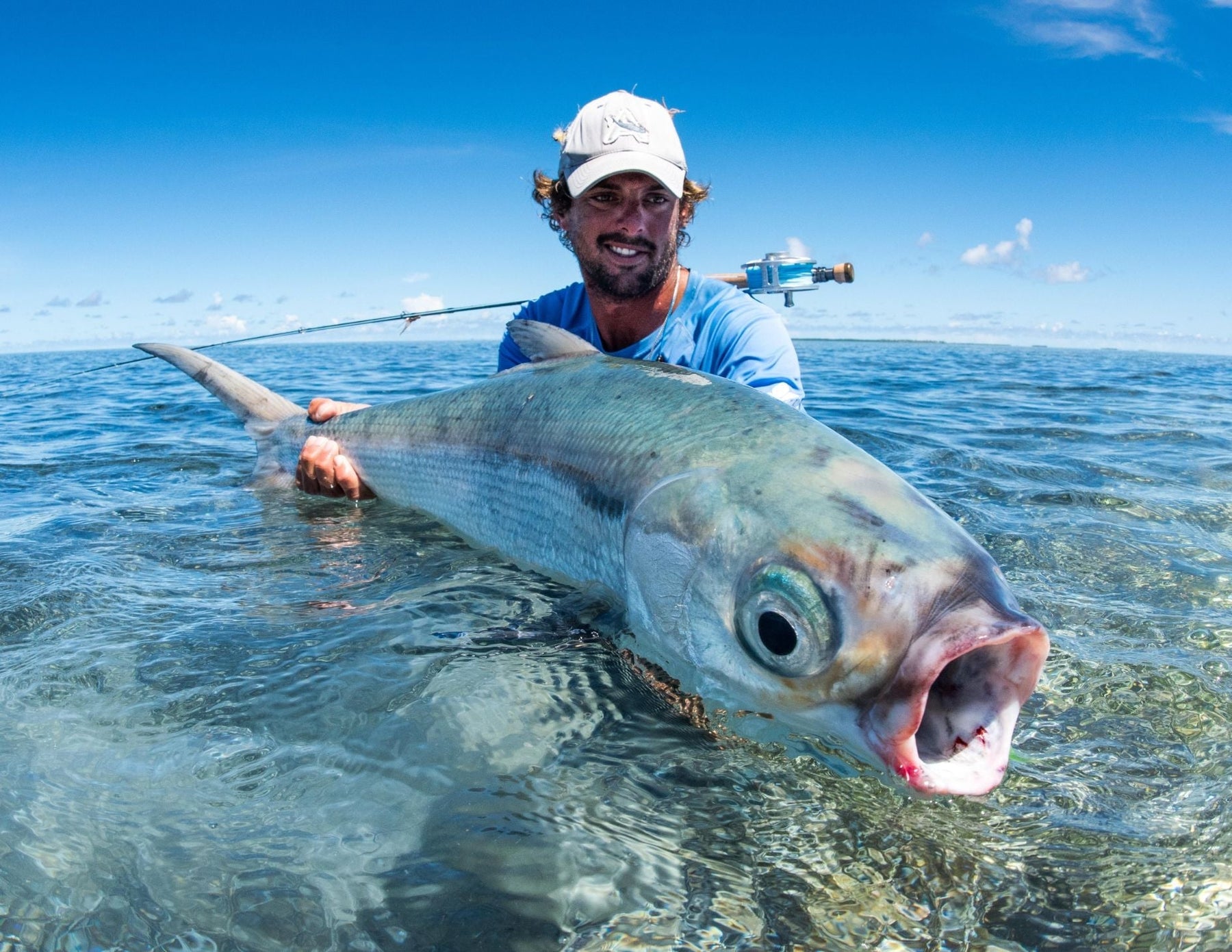 Jako Lucas holding a large milkfish in shallow tropical water with a fly rod