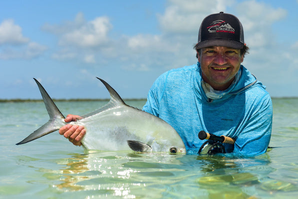 Angler holding a large silver fish in shallow Caribbean water beneath a blue sky