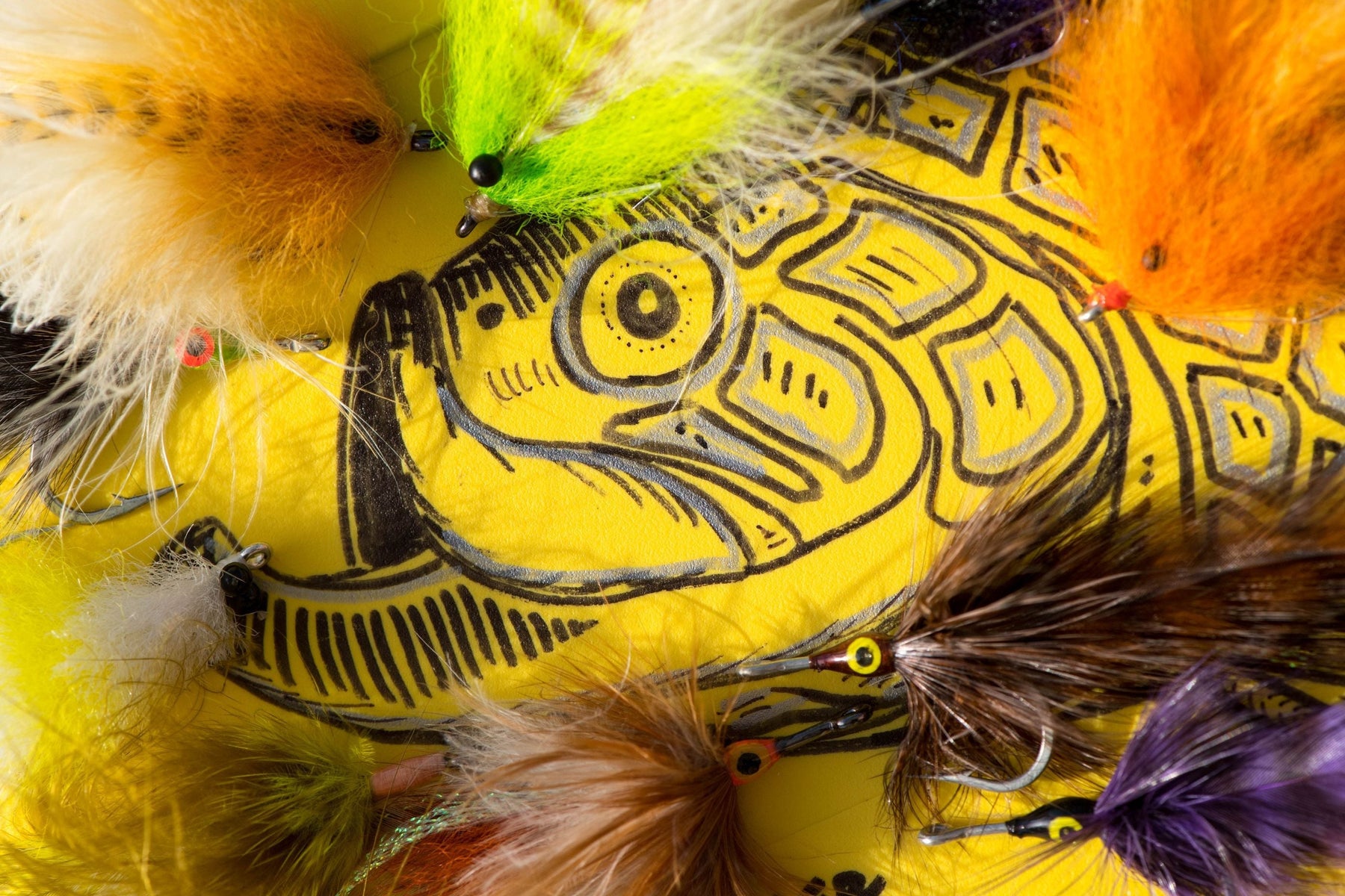 Close-up of colorful tarpon flies showcasing feathered designs on a yellow fish-patterned surface