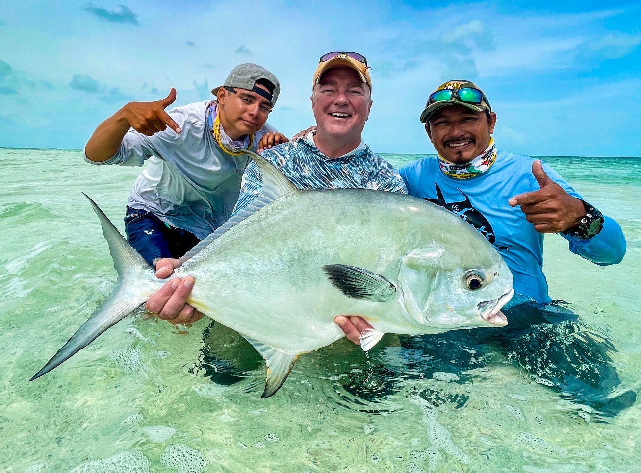 Three fly fishers holding a large silver fish in shallow tropical water