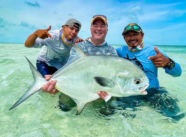 Three fly fishers holding a large silver fish in shallow tropical water
