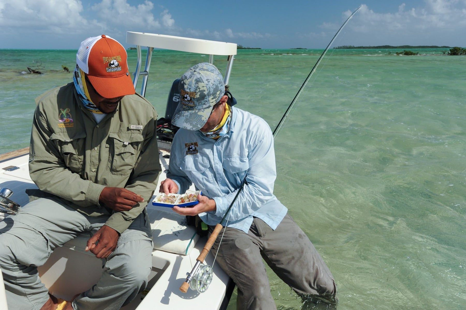 Two fly fishers examine flies aboard a boat in the shallow turquoise waters of The Bahamas