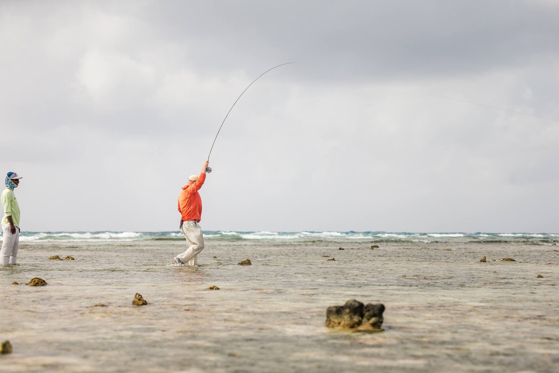 Fly fisher casting in shallow Belizean waters as a guide watches nearby