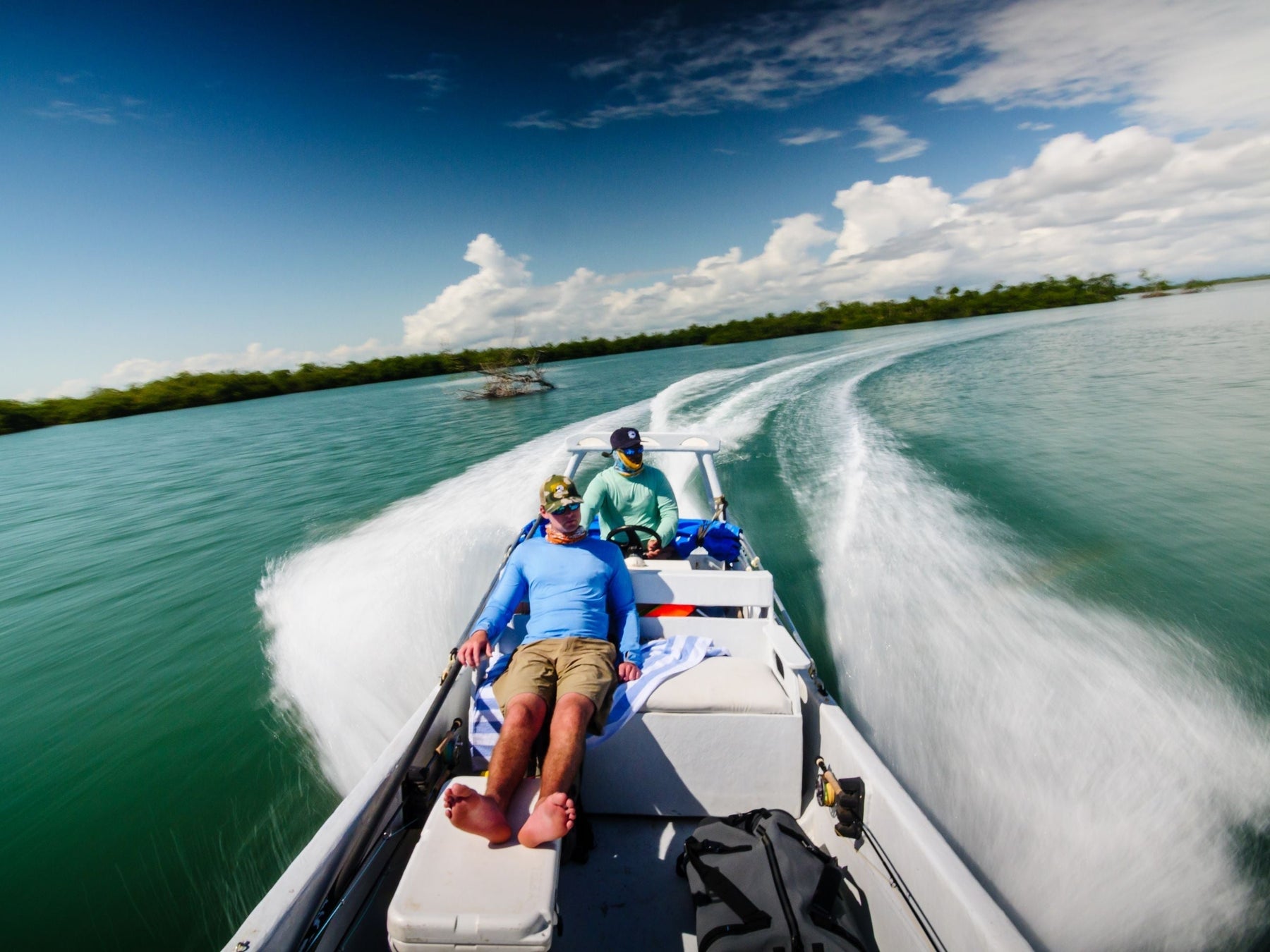Two people ride a speedboat through Belizean waters, leaving a wake beneath a sunny sky