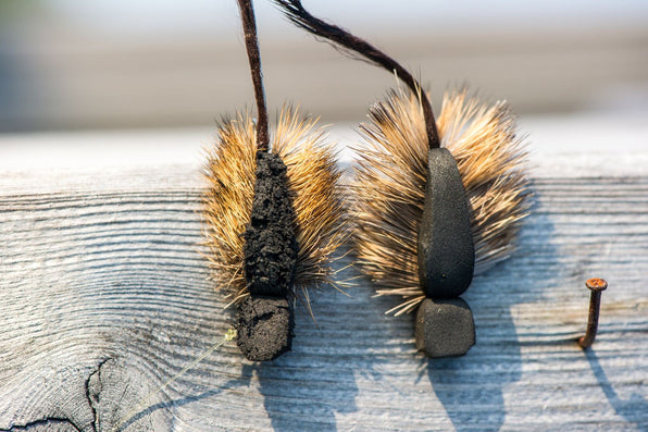 Close up of two fly fishing flies, mouse pattern, showing foam bodies and fur tails on weathered wooden plank