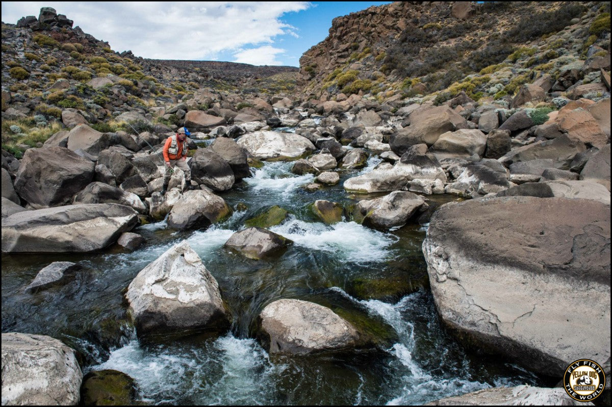 Fly fisher wades through the rocky Barrancoso River beneath rugged hills