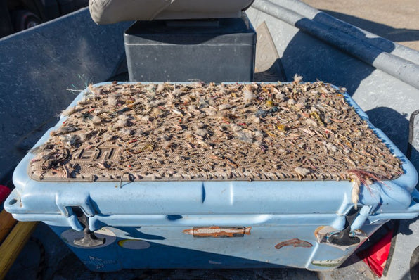 Top view of a fly box covered with assorted fly fishing flies on a boat