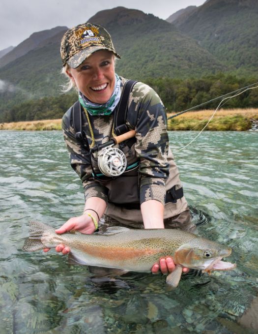 Angler holding a large trout in a New Zealand river with mountains in the background