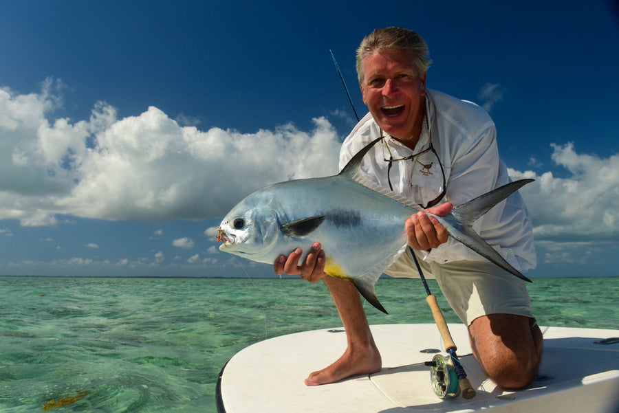 Smiling angler holding a large silver fish caught while fly fishing on a flats boat in shallow turquoise water under a blue sky