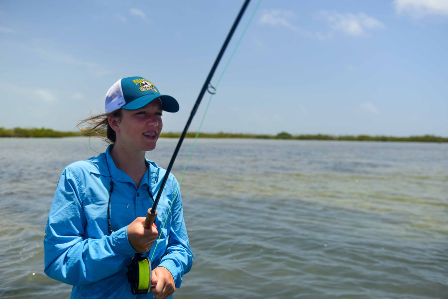 Teen girl casting a fly rod on shallow flats during a fly fishing trip, wearing a Yellow Dog cap and blue shirt