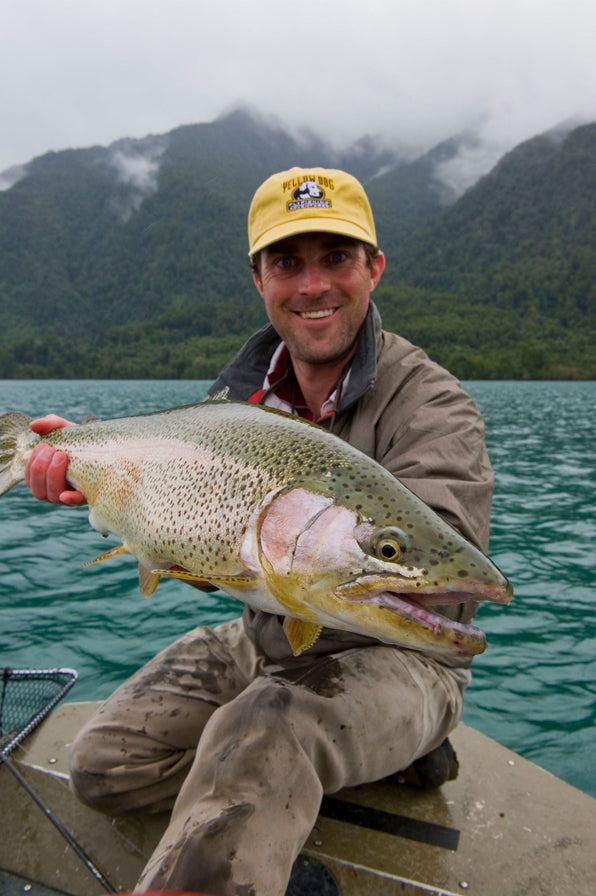 John Hudgens holding a large trout on a boat with misty mountains in the background