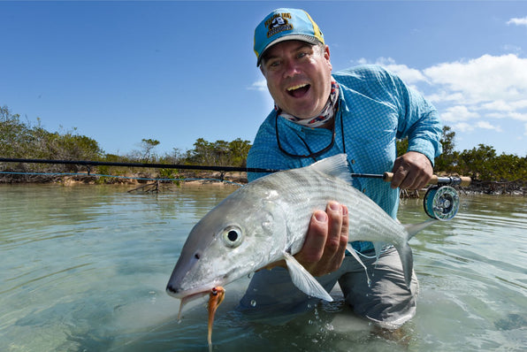 Angler holding a large bonefish while knee-deep in clear flats on Andros, Bahamas during a fly fishing trip