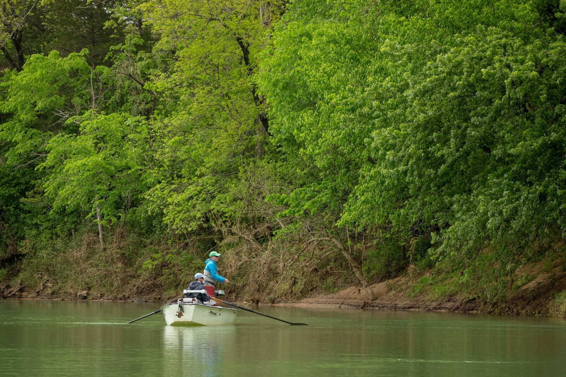 Two anglers fish from a small boat on a wooded Arkansas river