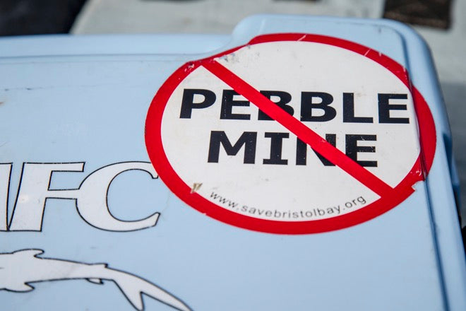 Round sticker reading PEBBLE MINE with red circle and diagonal slash on a light blue cooler, savebristolbay.org visible
