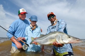 Three fly-fishing anglers holding a large snook in shallow water off Punta Allen, Mexico