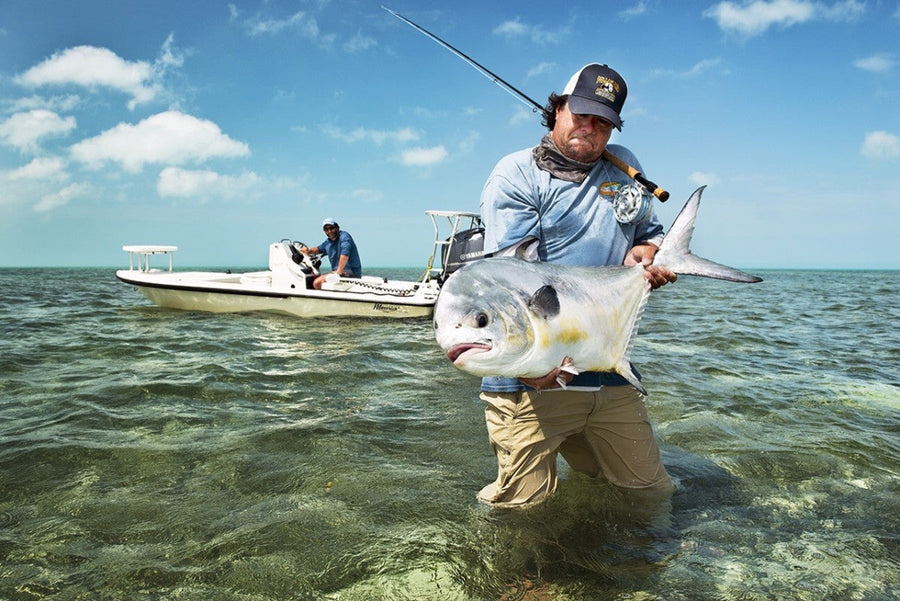 Angler holding a large permit while wading Florida flats on a fly fishing trip, skiff and crew in the background