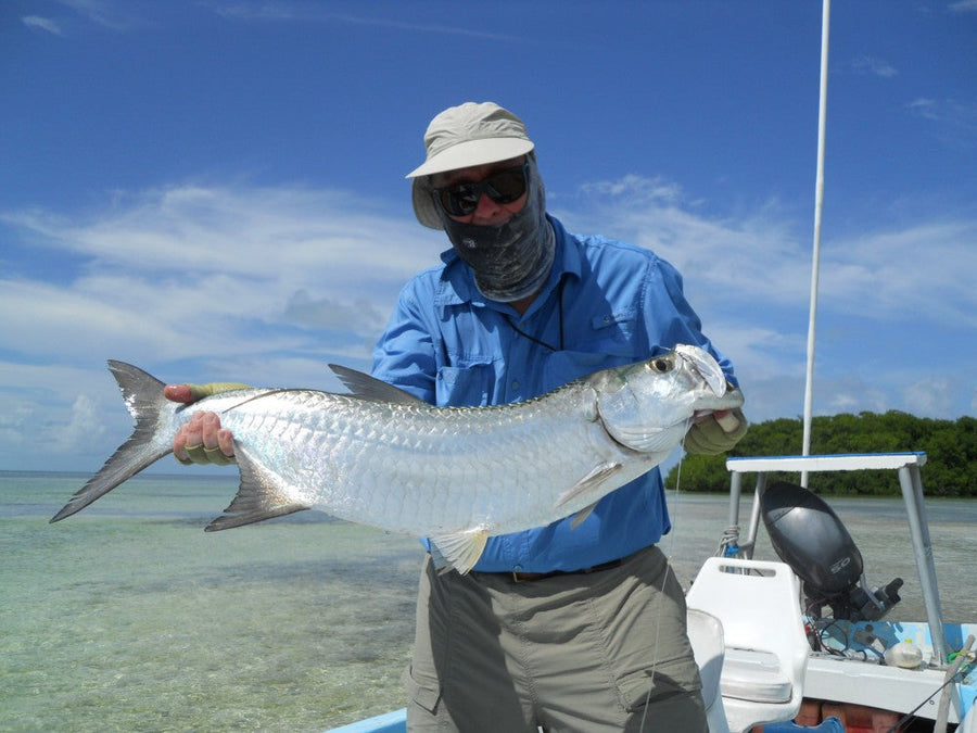 Angler holding a large tarpon on a flats skiff in shallow turquoise water during a Yucatan fly fishing trip