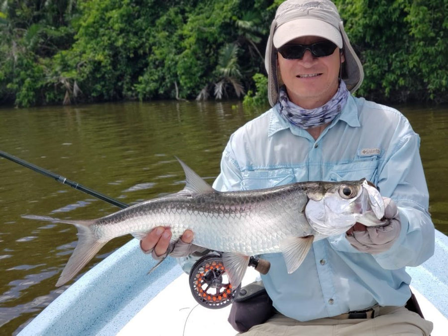 Angler holding a tarpon while seated in a skiff on a mangrove-lined river during a fly fishing trip