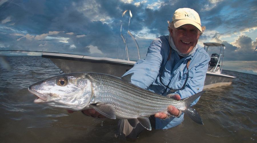 Angler holding a large bonefish in shallow water beside a skiff during a Bahamas fly fishing trip