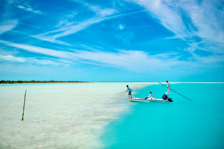 Two guides poling a skiff while an angler casts on shallow turquoise flats at Mangrove Cay Club, Bahamas