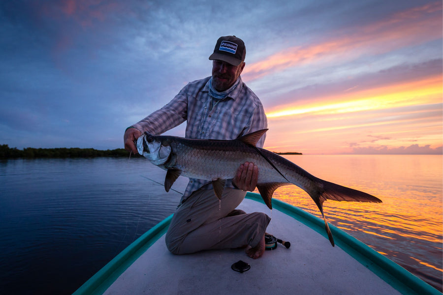 Angler holding a large tarpon on the bow of a skiff at sunset during a fly fishing trip in Mexico