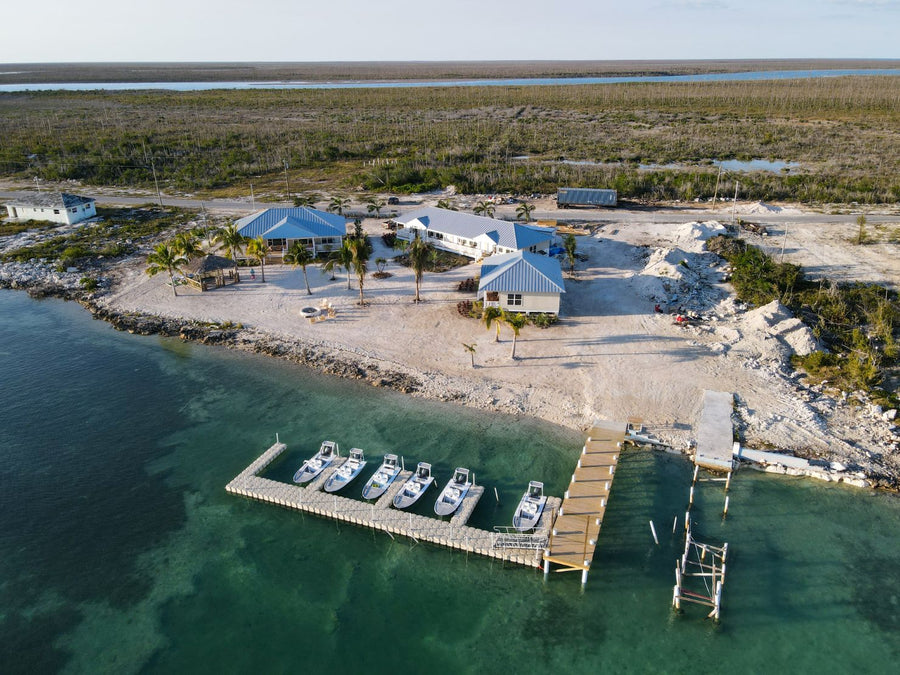Aerial view of East End Lodge on a Bahamian shoreline with a dock and six skiffs lined up for fly fishing trips