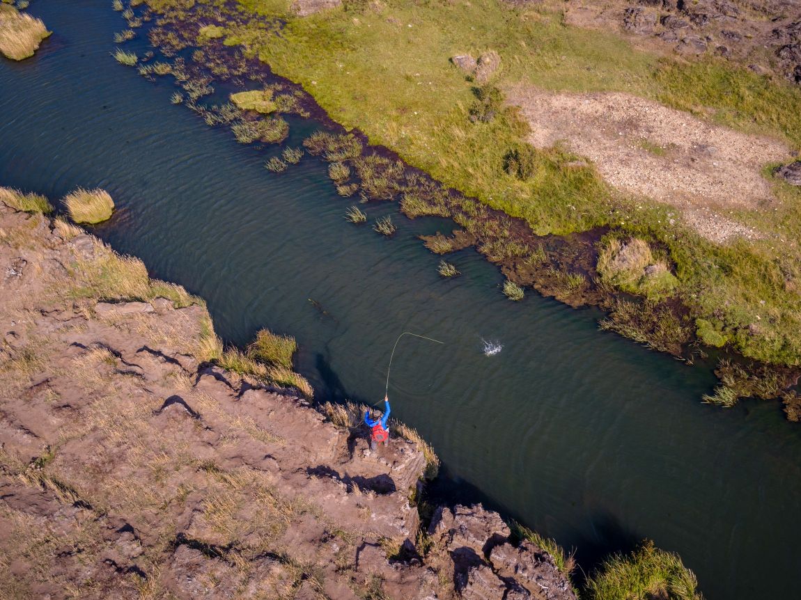 Aerial view of an angler fly fishing in a river surrounded by rugged grassy banks in Argentina