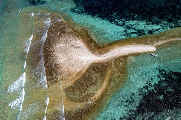 Sandy Seychelles sandbar surrounded by turquoise water and coral reefs with a small boat nearby