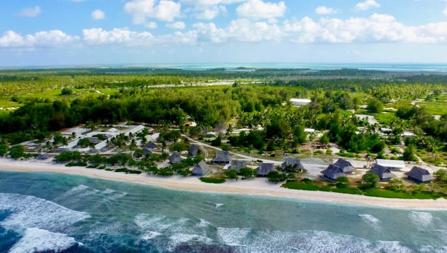 Christmas Island Lodge beachfront bungalows along a sandy shore with palm trees and turquoise reef-lined ocean, aerial view