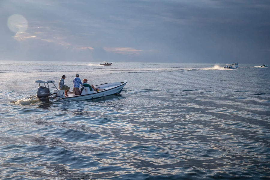 Three anglers on a skiff preparing gear on calm ocean at dawn during a fly fishing trip
