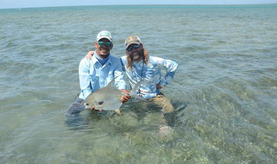 Two anglers wading in shallow clear water holding a permit fish on a fly fishing trip in the Faraway Cayes