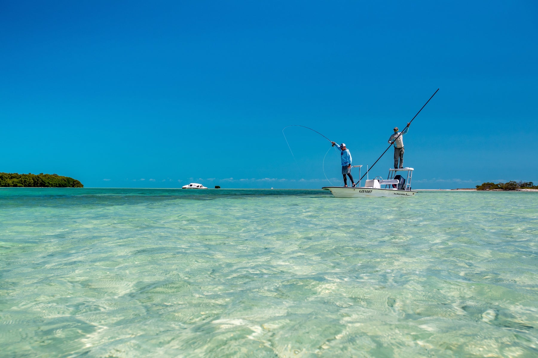 Two anglers fly-fishing from a flats boat in shallow turquoise water
