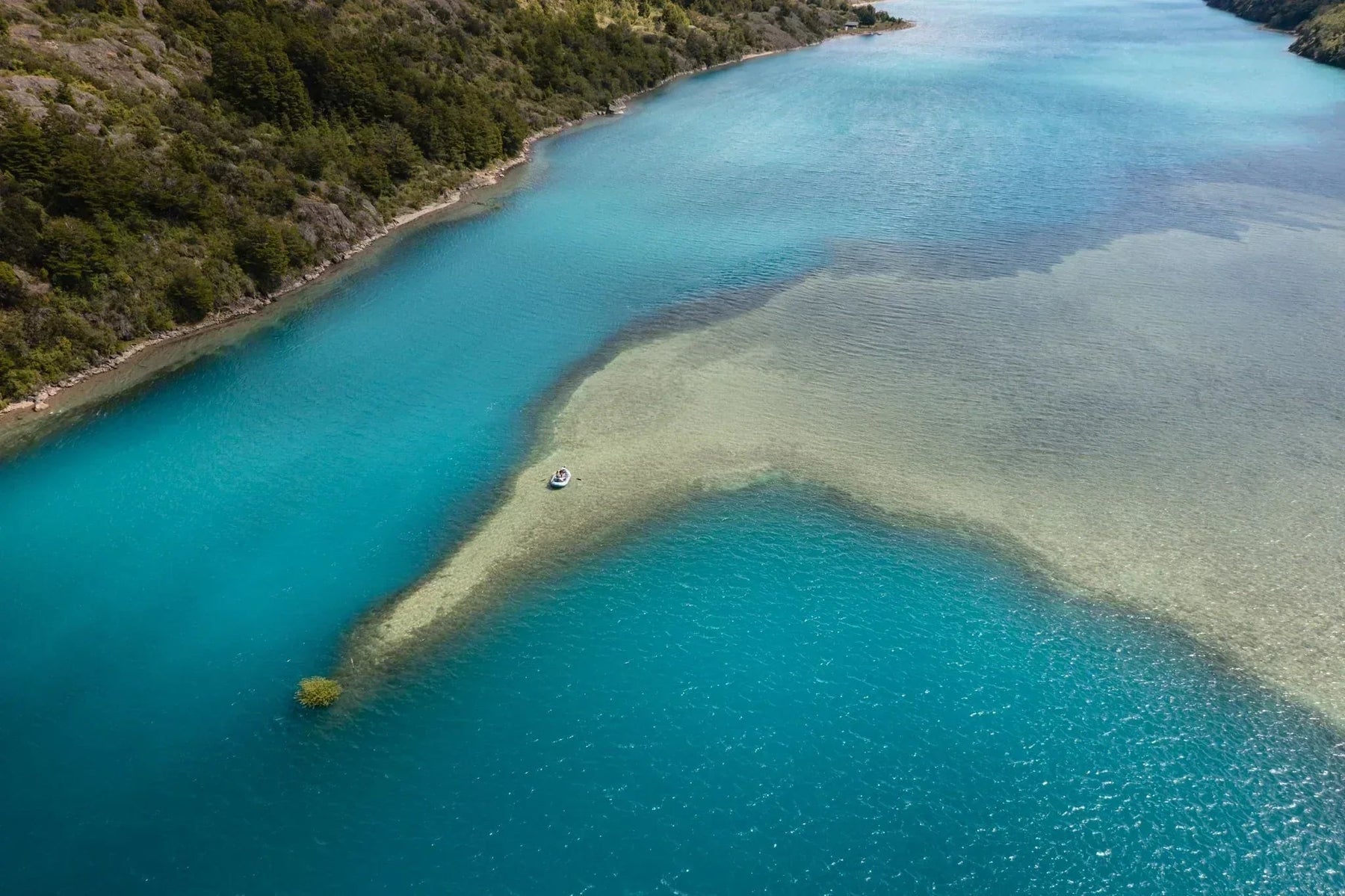 Aerial view of turquoise lake waters, wooded rocky shoreline, and a small boat in Patagonia