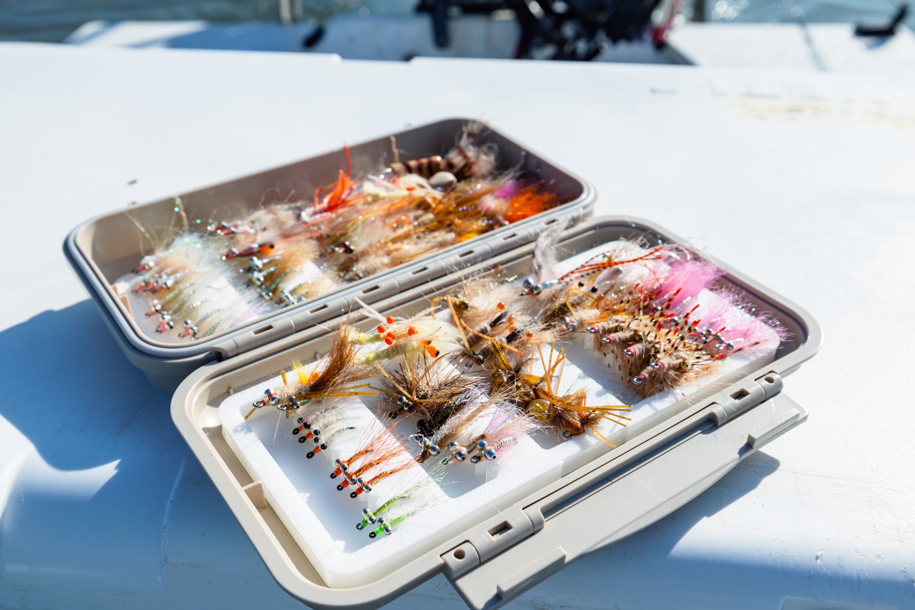 Close-up of bonefish flies in two open fly boxes showcasing assorted colors and patterns on a boat deck