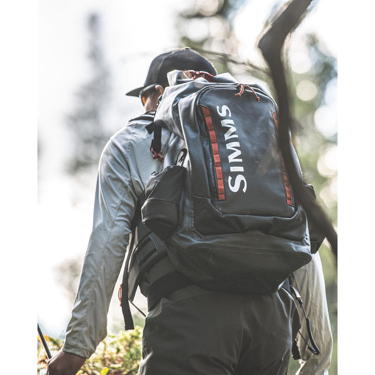 Rear view of Simms G3 Guide Backpack in Anvil showcasing roll top waterproof design and padded hipbelt on angler in forest
