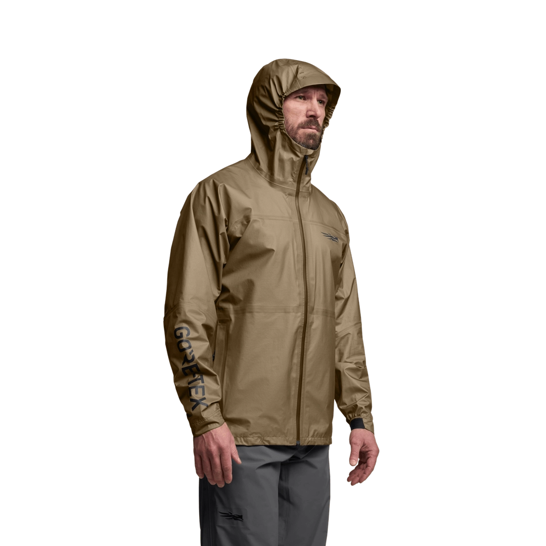 Three-quarter view of SITKA Dew Point UL Jacket on male model, hood up, tan color, GORE-TEX logo on sleeve, white background