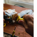 Loon Outdoors Ergo Hair Packer in yellow held in hand packing hair into a fly vise, showing ergonomic handle and bristle head