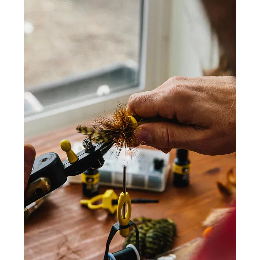 Hand using Loon Outdoors Ergo Hair Packer to compress deer hair on a fly in a vise on a wooden workbench
