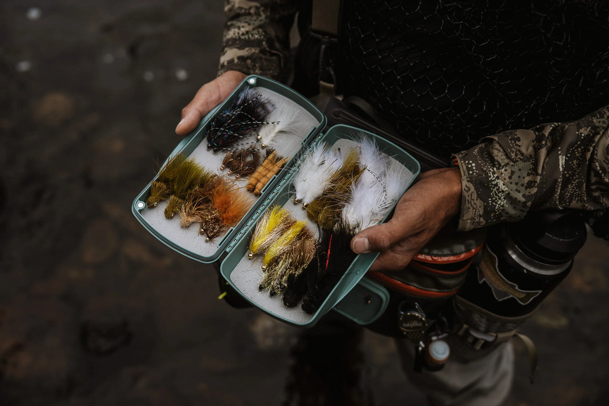 Angler holding open Fishpond Tacky Pescador large fly box with Dynamic Foam insert full of assorted flies over a river