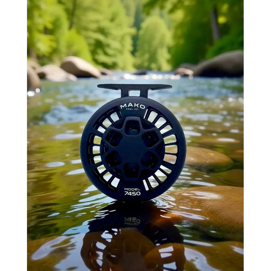 Front view of Mako 7450 freshwater fly reel showcasing large-arbor spool and matte black finish on a river rock in a shallow stream