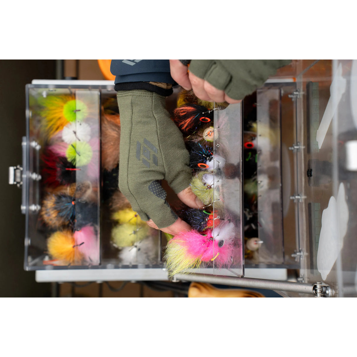 Top-down view of olive Skwala Thermo 300 fingerless glove on a hand showing textured grip pads reaching into a clear fly box