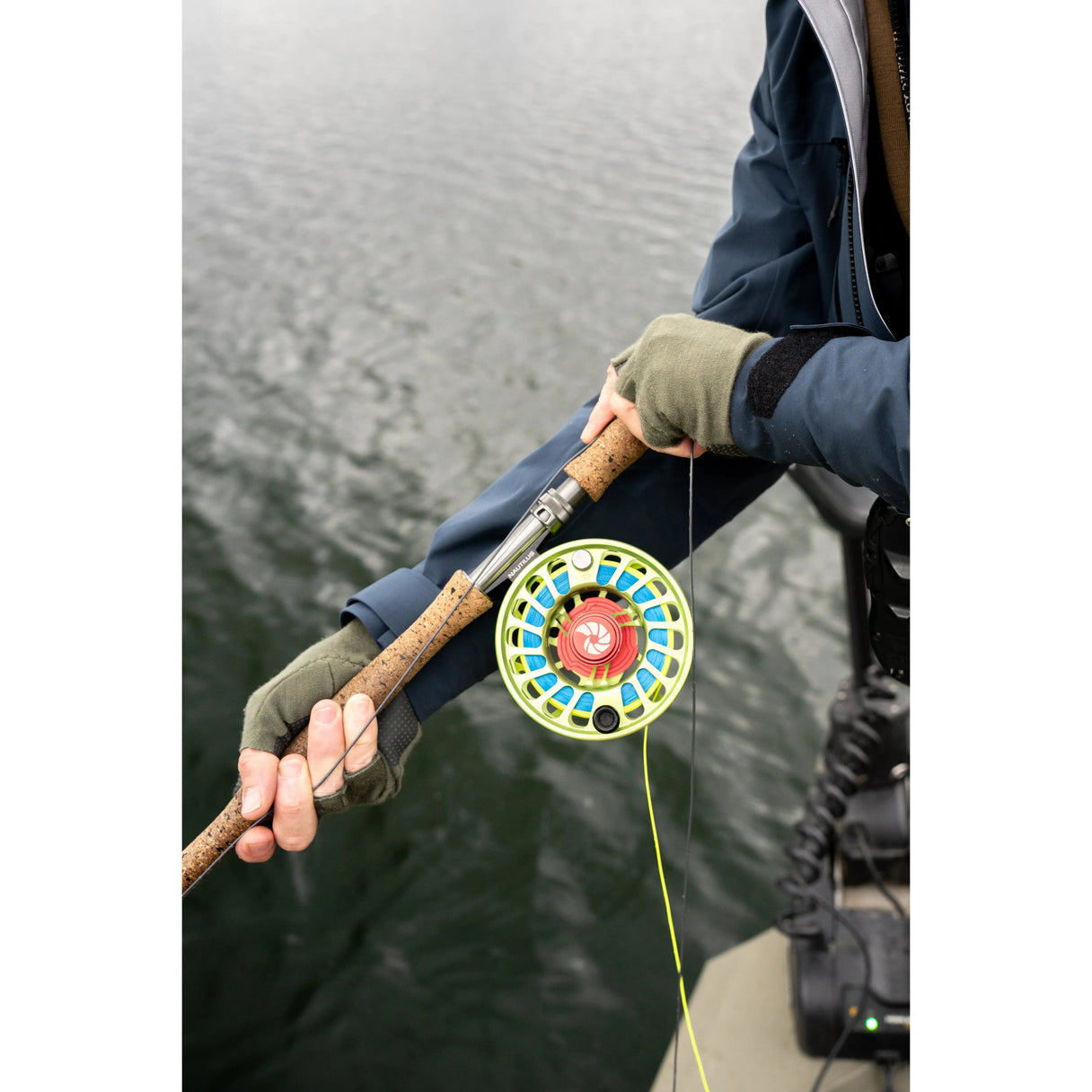 Close-up of Skwala Thermo 300 fingerless gloves in Tent green showing knit 300-weight Merino fabric and reinforced palms as hands hold a fly rod over water